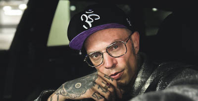 Tattoed Man sits in car and wears Crown Chakra Snapback Cap in digital lavender / black